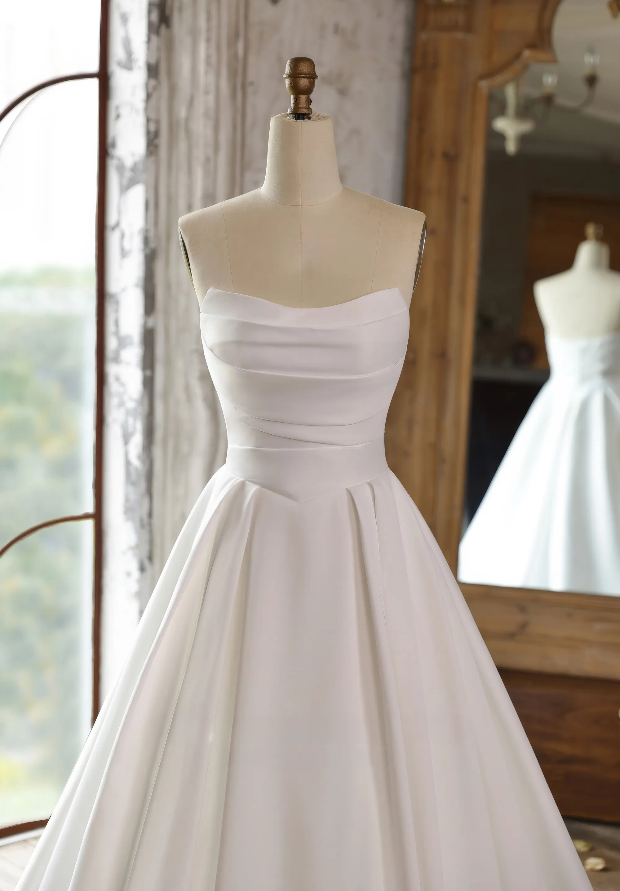 Ein schlichtes Brautkleid hängt an einer Schneiderpuppe in einem rustikalen Raum, Front Close-up