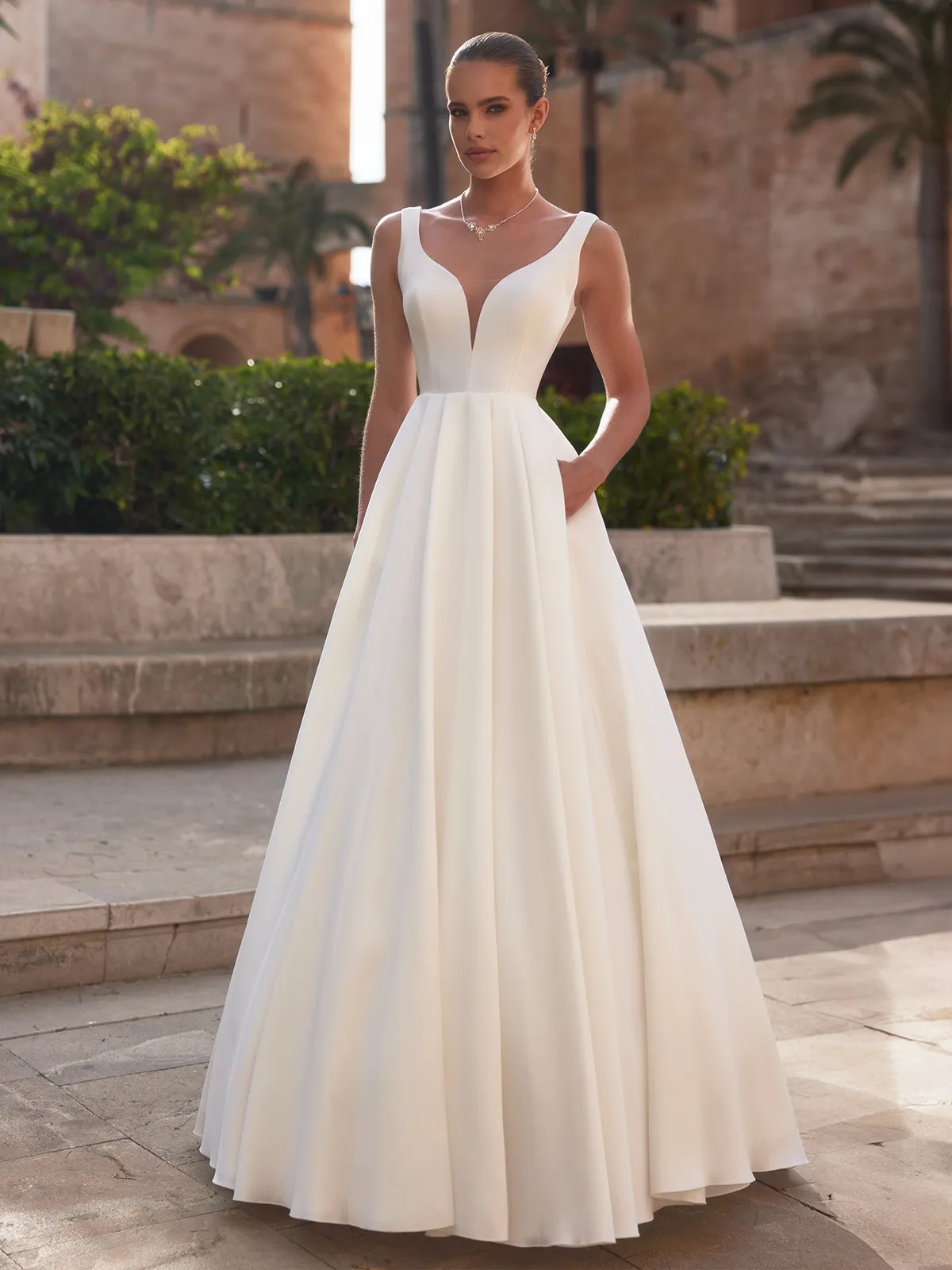Schlichtes Hochzeitskleid Idalia mit Taschen Braut in einem schlichten Hochzeitskleid aus Mikado, mit V-Ausschnitt, eine Hand in einer seitlichen Tasche