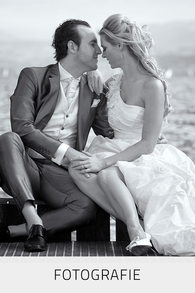 Brautpaar-Fotografie von einem Brautpaar am See sitzend, die Braut in einem One-shoulder Brautkleid