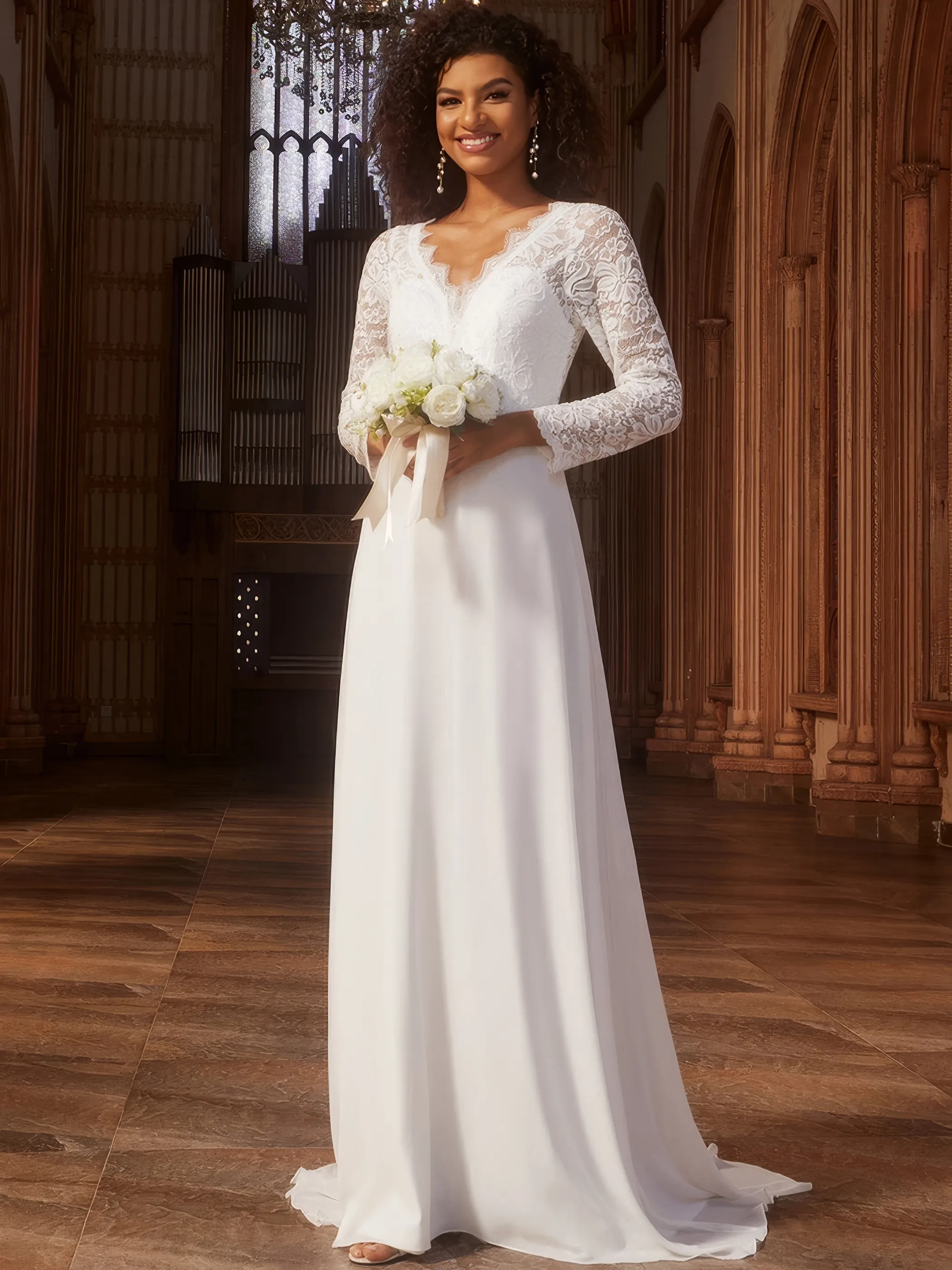 Dunkelhäutige Braut in einem elfenbeinfarbigen Brautkleid aus Spitze und mit langen Ärmeln