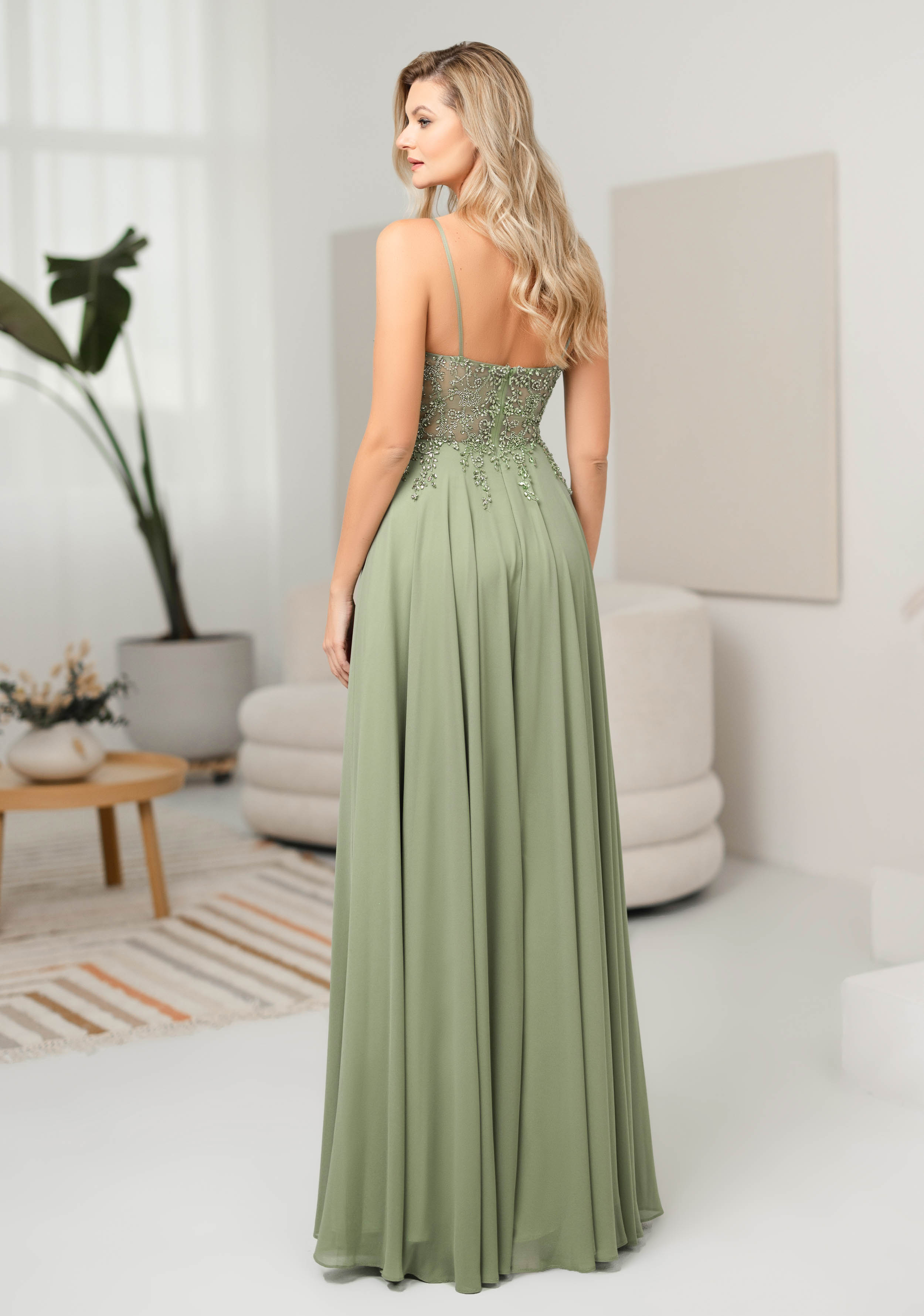 Frau in einem langen Abendkleid mit halbtransparentem Oberteil in der Farbe Lindengrün, Rückenansicht
