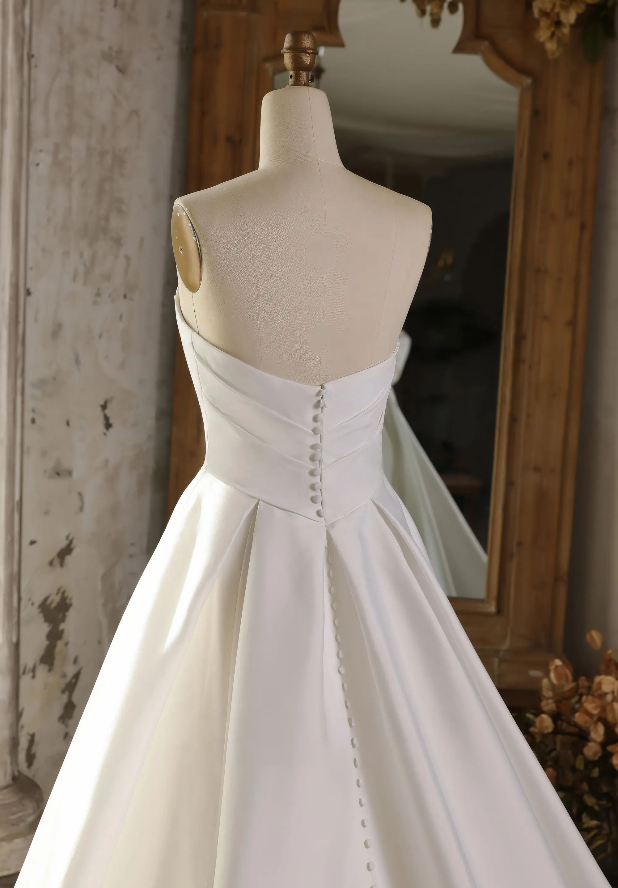 Ein schlichtes Brautkleid hängt an einer Schneiderpuppe in einem rustikalen Raum, Rücken Close-up