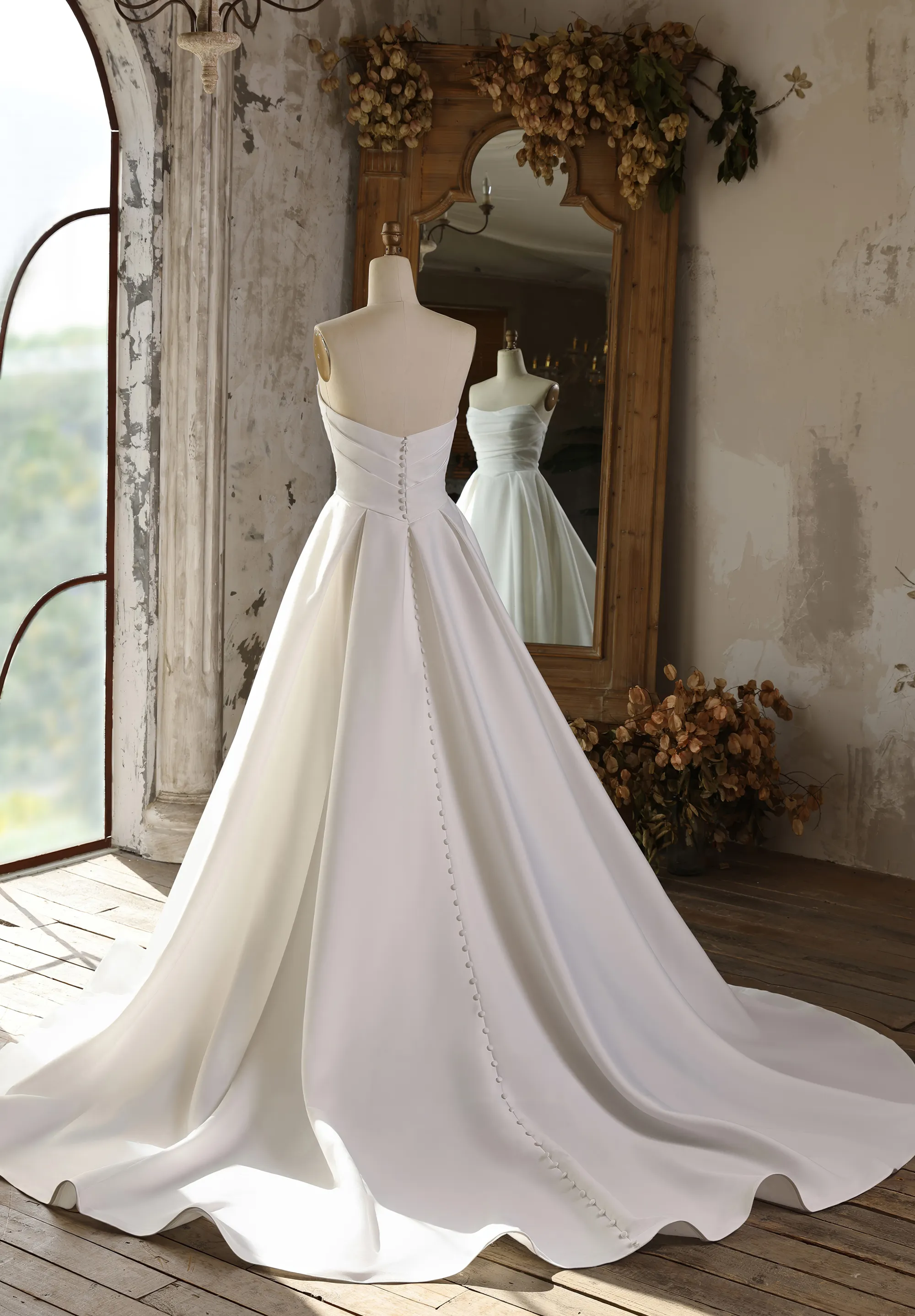 Ein schlichtes Brautkleid hängt an einer Schneiderpuppe in einem rustikalen Raum, Rückenansicht