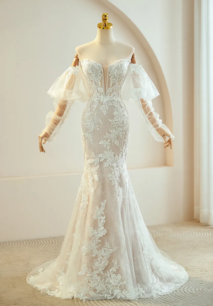 Meerjungfrau-Brautkleid mit tiefem Herzausschnitt, abnehmbaren Off-Shoulder-Tüllärmeln, Korsett-Mieder und vollständig mit floraler Spitze bedecktem Rock in Champagner – individuelles Brautkleid-Detail Trend 2026