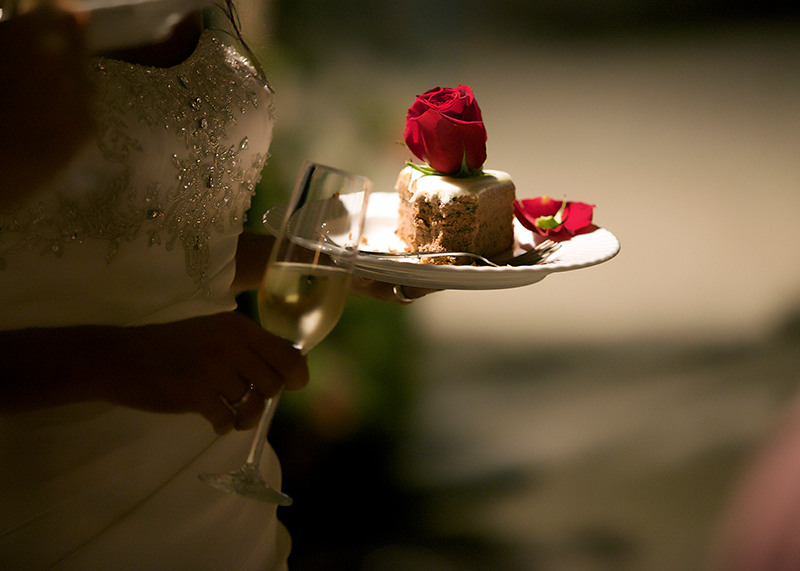 Eine Braut hält einen Teller mit einem Stück Hochzeitstorte und ein Champagnerglas
