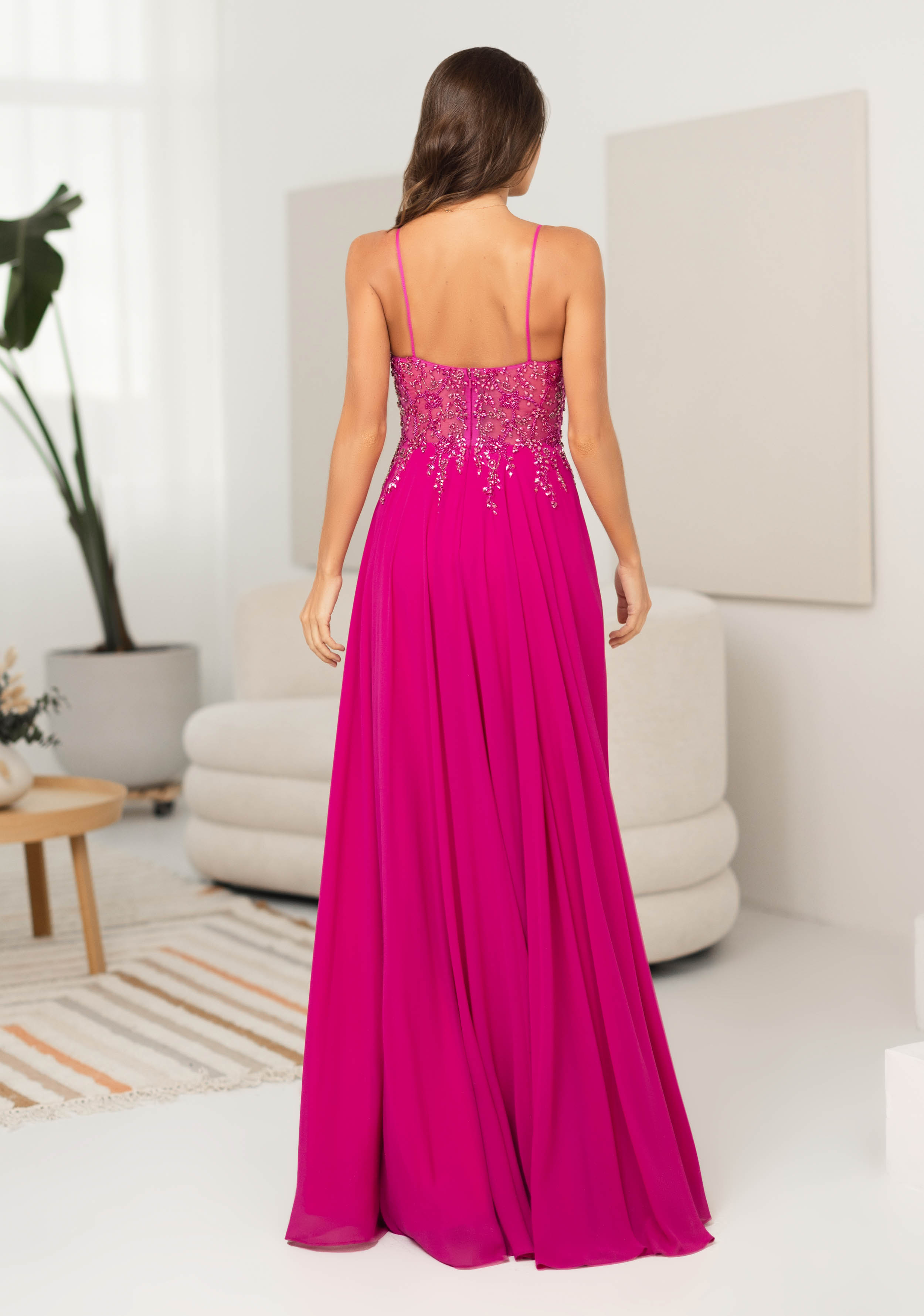 Frau in einem langen Abendkleid mit halbtransparentem Oberteil in der Farbe Shocking Pink, Rückenansicht