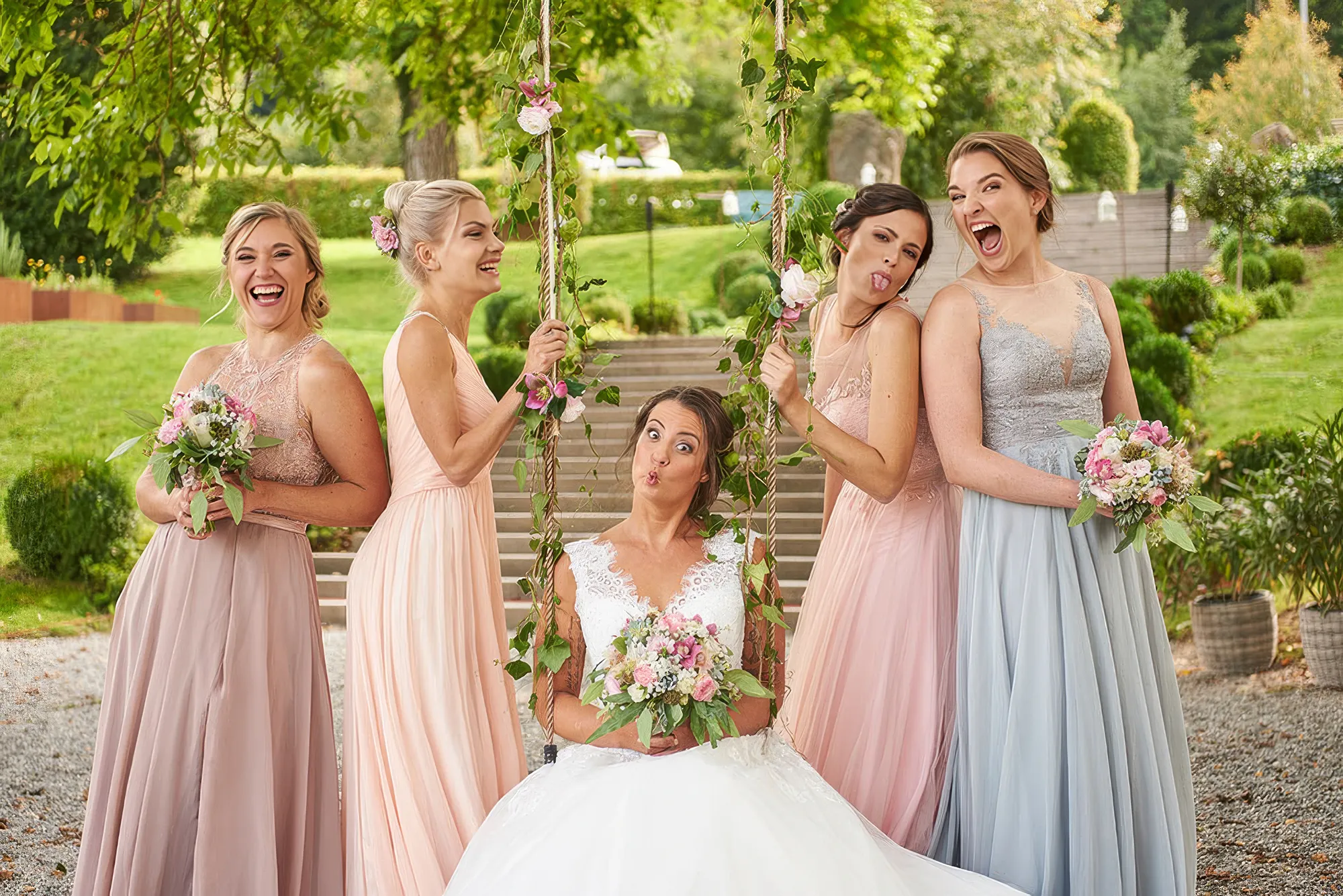 Eine Braut sitzt auf der Schaukel, links und rechts zwei Brautjungfern in Brautjungfernkleider