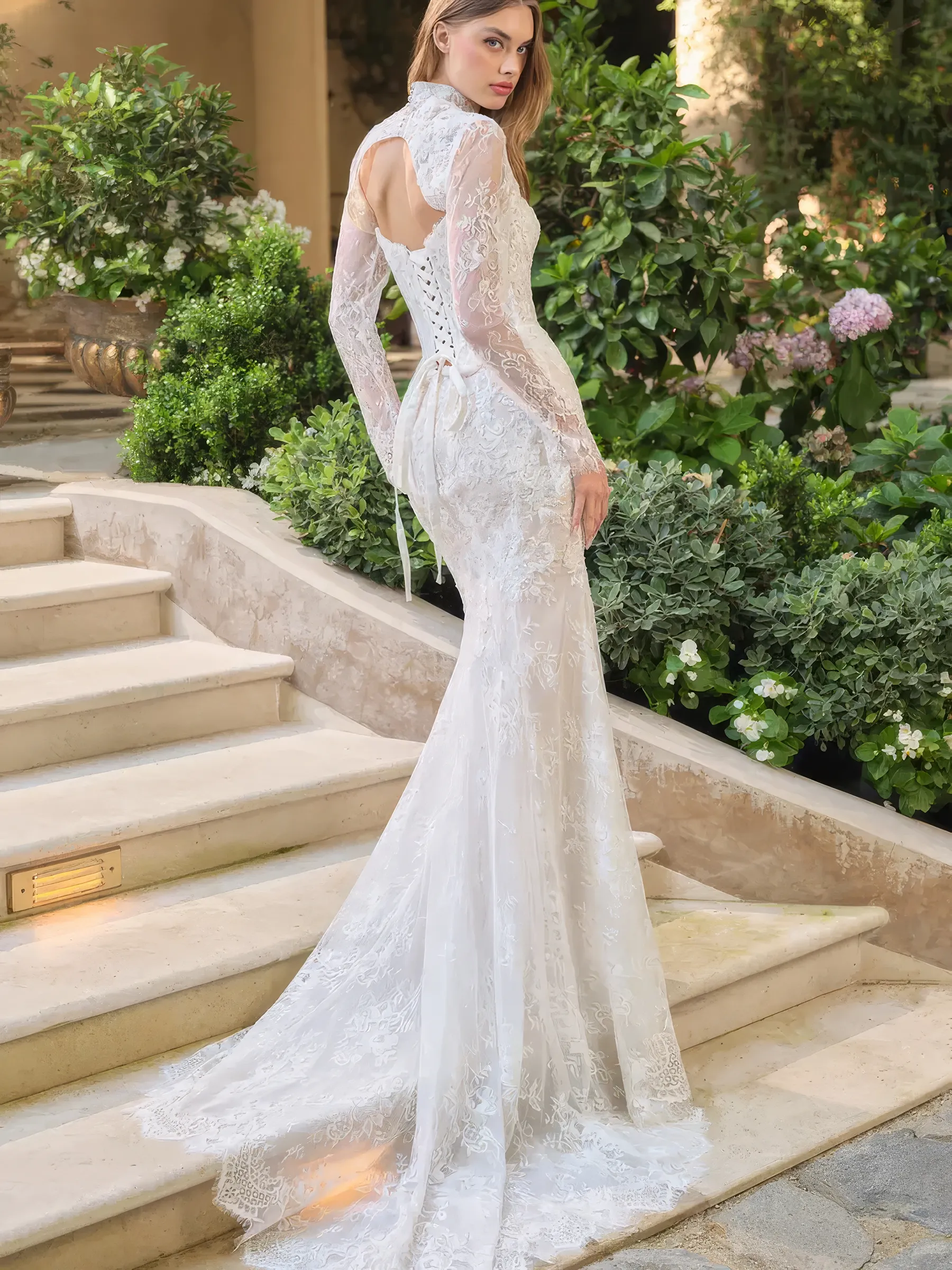 Rückansicht des Brautkleids in Off-White – Schnürkorsage am Rücken des Grundkleids, offener Bolero-Rücken mit langen Spitzenärmeln und florale Spitzenschleppe im Fit & Flare-Schnitt.